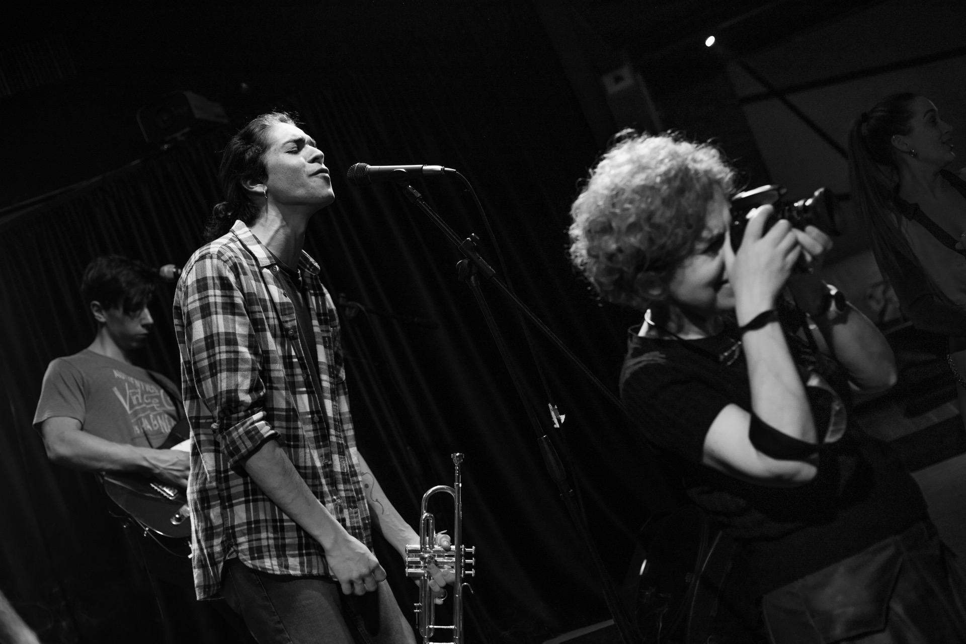 Singer performing, trumpet player and photographer in background, black and white